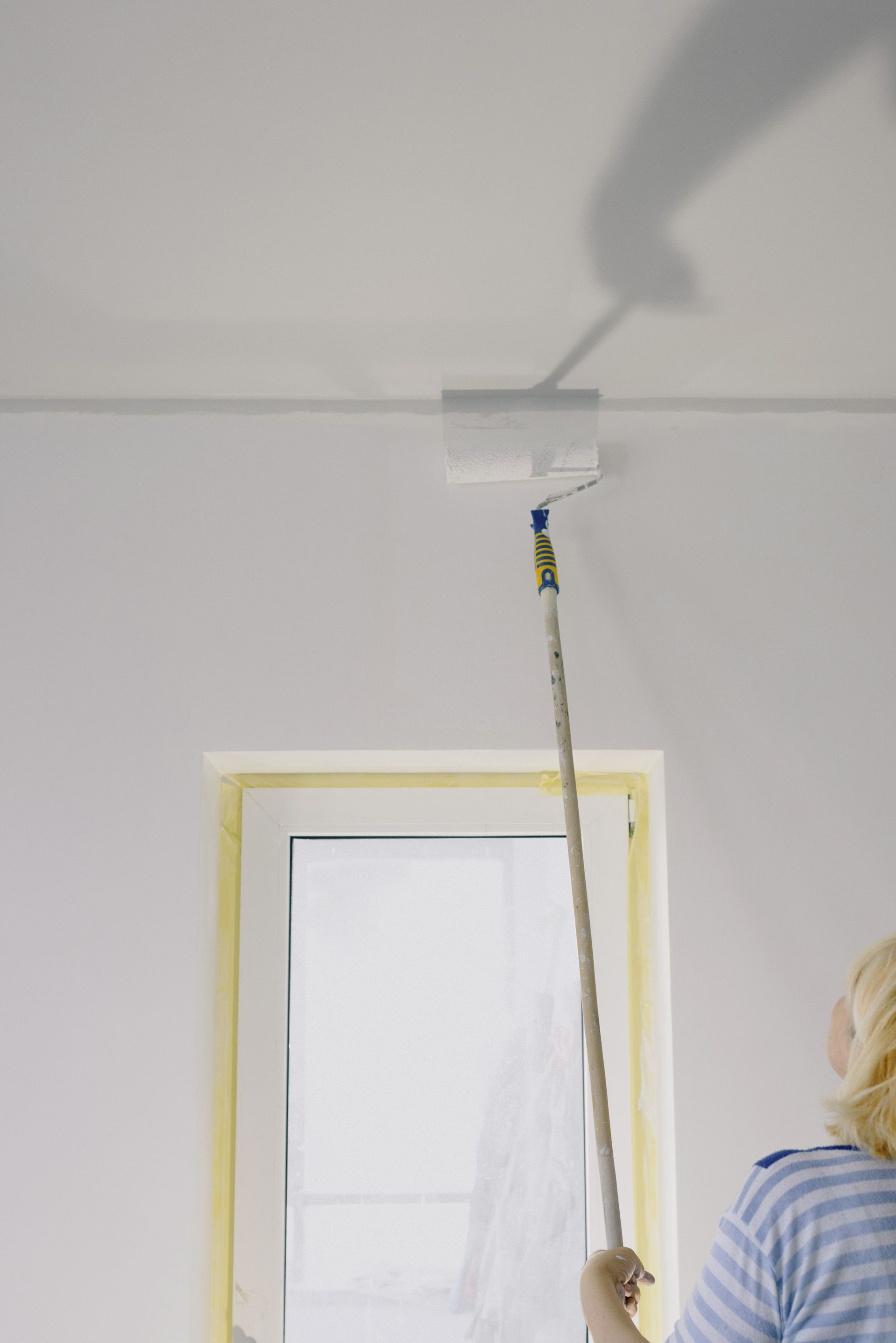 Crop faceless female holding paint roller and renovating walls in room at home